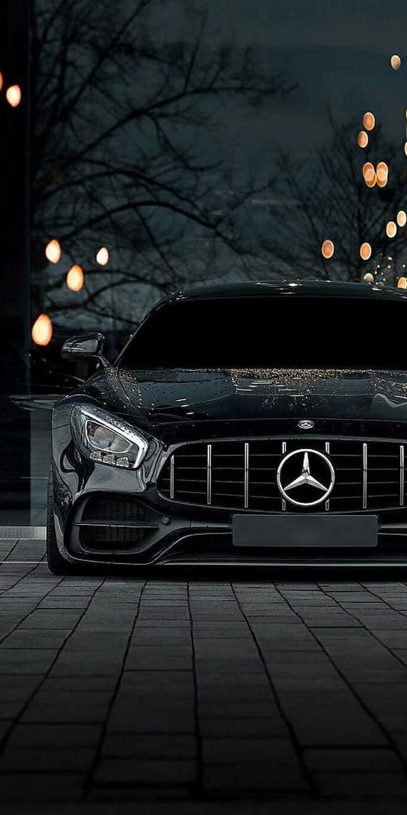 Mercedes-AMG GT sports car front view with LED headlights and a silver emblem on wet pavement at night.