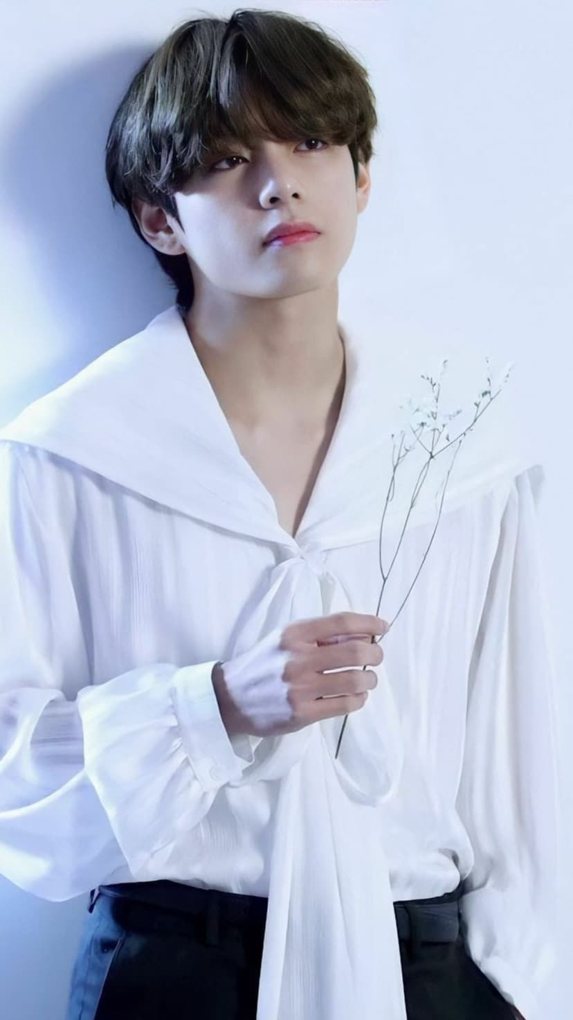 Kim Taehyung holds a small sprig of white flowers while wearing a collared white shirt with a front bow.
