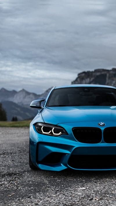 Blue BMW M2 parked on gravel with mountains background