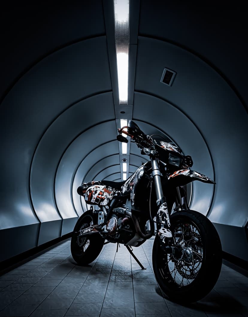 Supermoto motorcycle with custom decals parked inside a modern white tunnel featuring bright overhead lights.