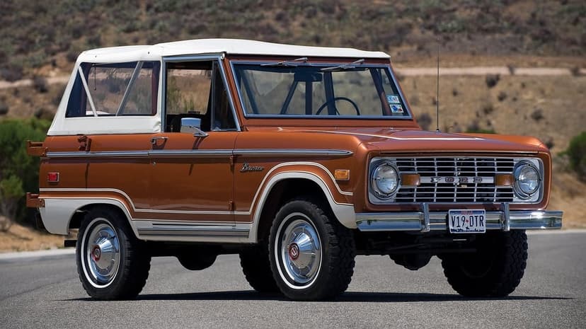 Copper vintage Ford Bronco with white soft top parked on an asphalt road with a blurred desert hill background.