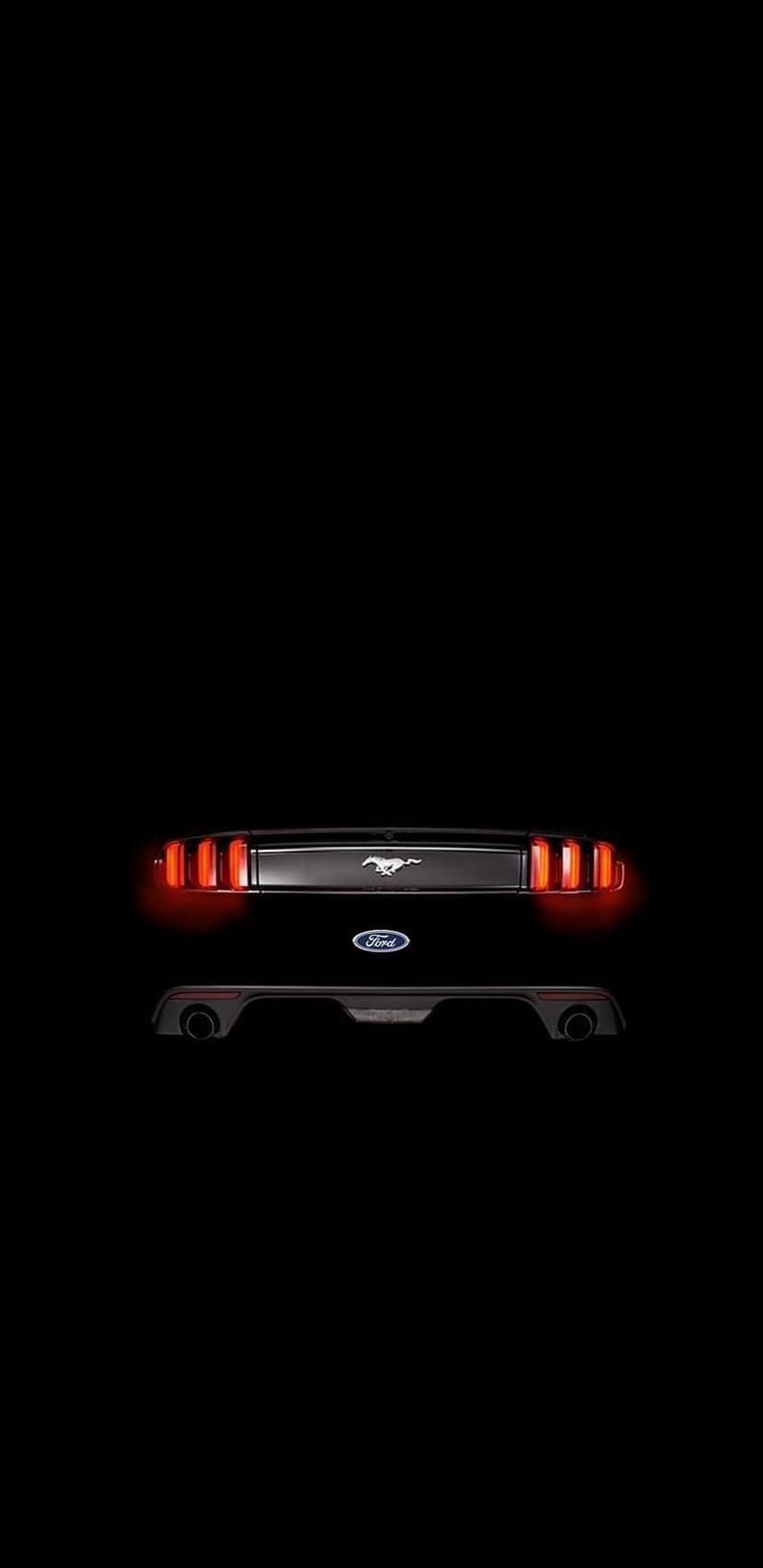 Red vertical tail lights and a chrome galloping horse emblem shine on the rear of a black car at night.