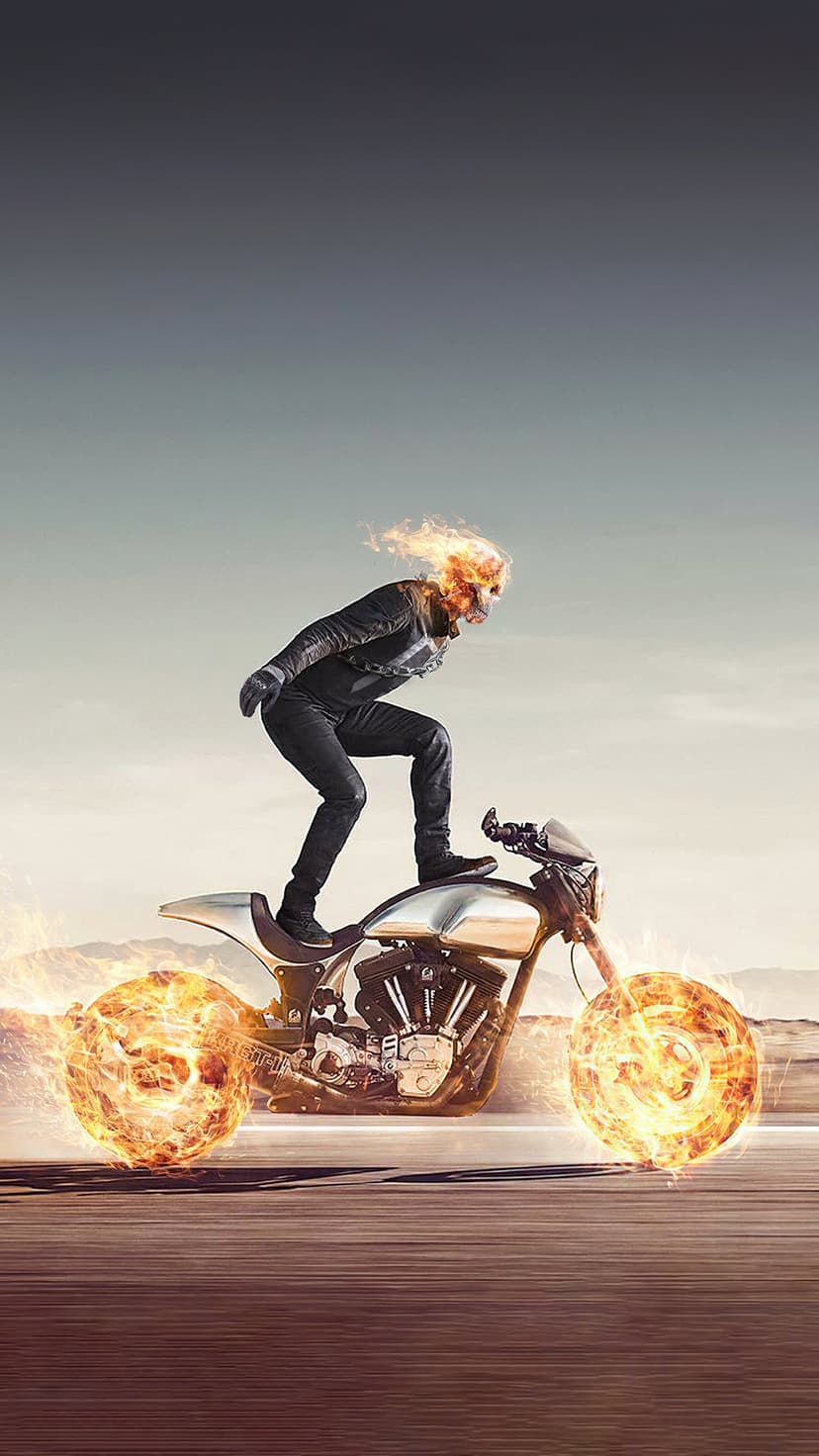 Ghost Rider on a motorcycle with wheels of fire drives across a dusty desert road under a hazy, orange-tinted sky.