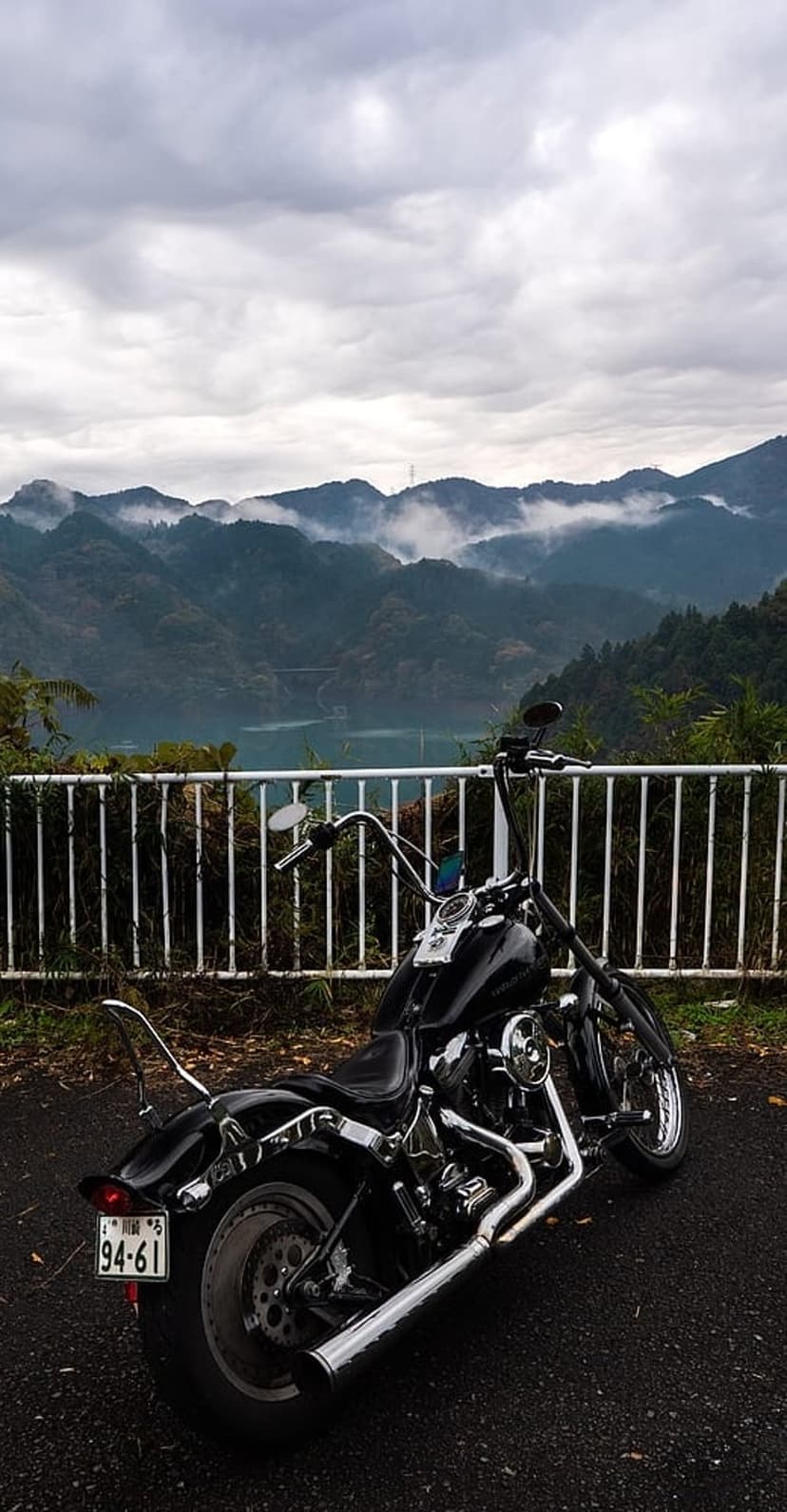 Black cruiser motorcycle parked by a white fence with a background of misty blue mountains and a serene lake.
