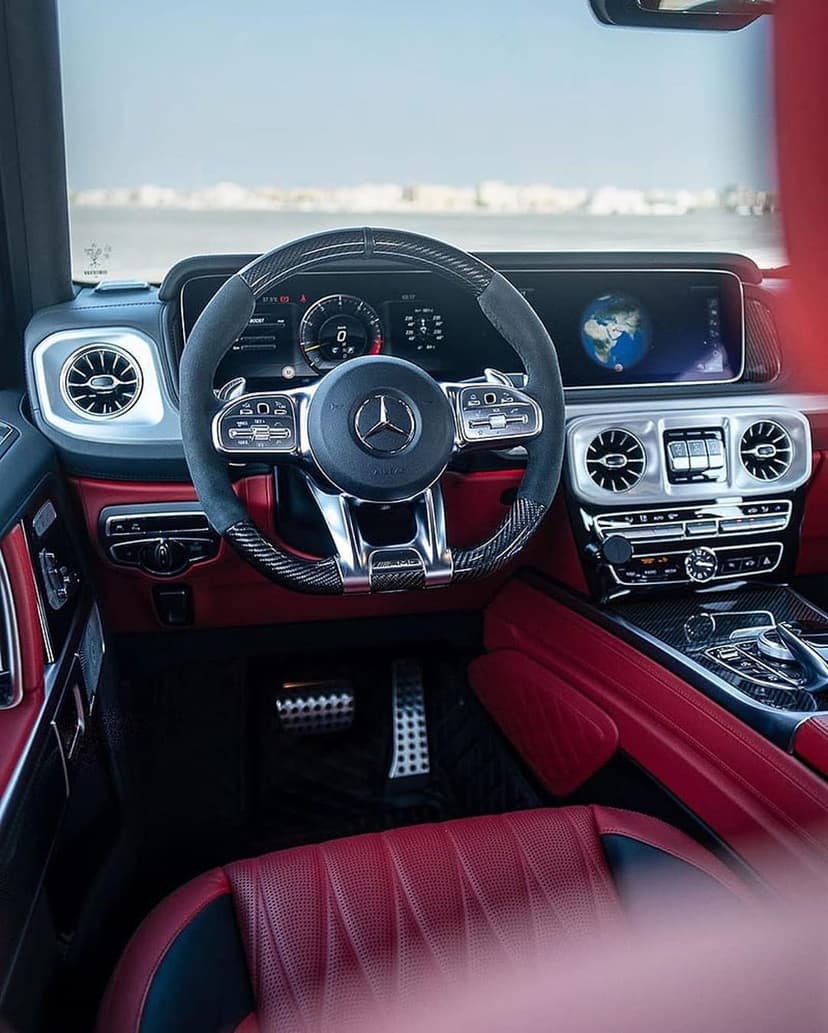 Red Mercedes G-Wagon interior featuring a carbon fiber steering wheel and digital infotainment dashboard screen.