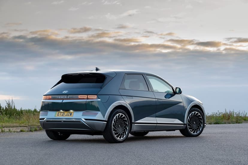 Rear view of a dark teal Hyundai IONIQ 5 on an asphalt road with pixelated LED taillights under a sunset sky.