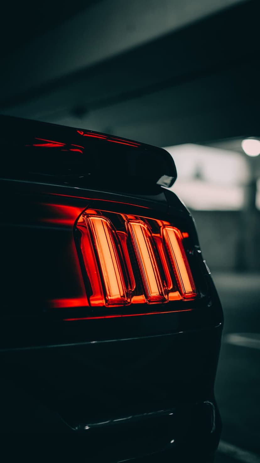 Red vertical LED tail lights of a Ford Mustang glow intensely within the shadows of a dark concrete parking garage.