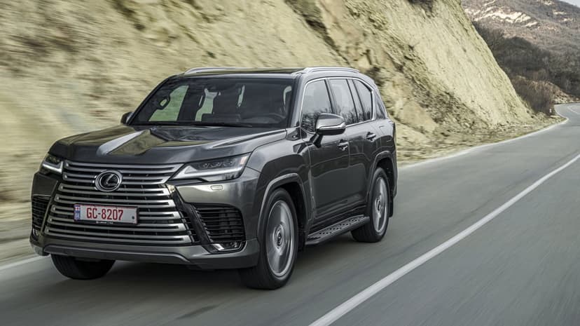 Charcoal grey Lexus LX SUV driving on a winding road next to a tall, textured rocky cliff face.