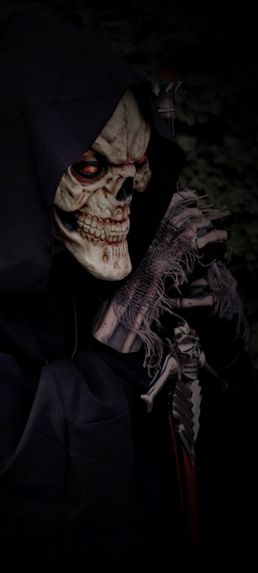 Grim reaper with glowing red eyes grips a silver sword, wearing tattered black robes and a weathered skull mask.