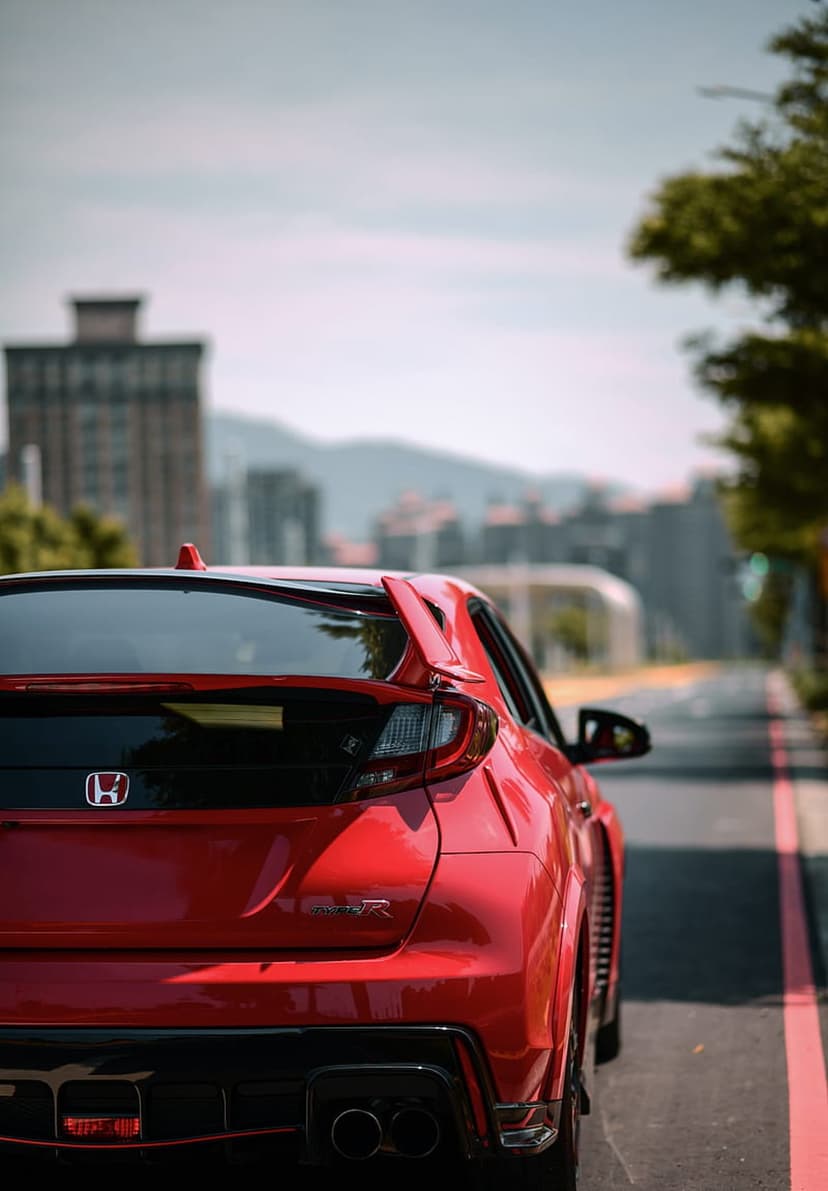 Red Honda Civic Type R parked on asphalt featuring a large rear wing and dual exhaust pipes in a city setting.