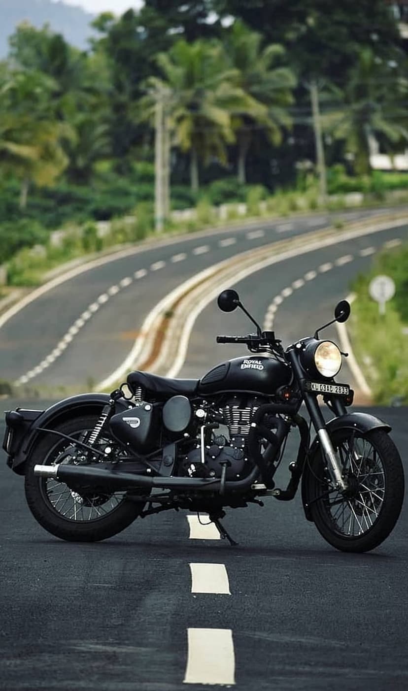 Royal Enfield motorcycle with chrome accents parked on a curving asphalt road surrounded by dense green forest.