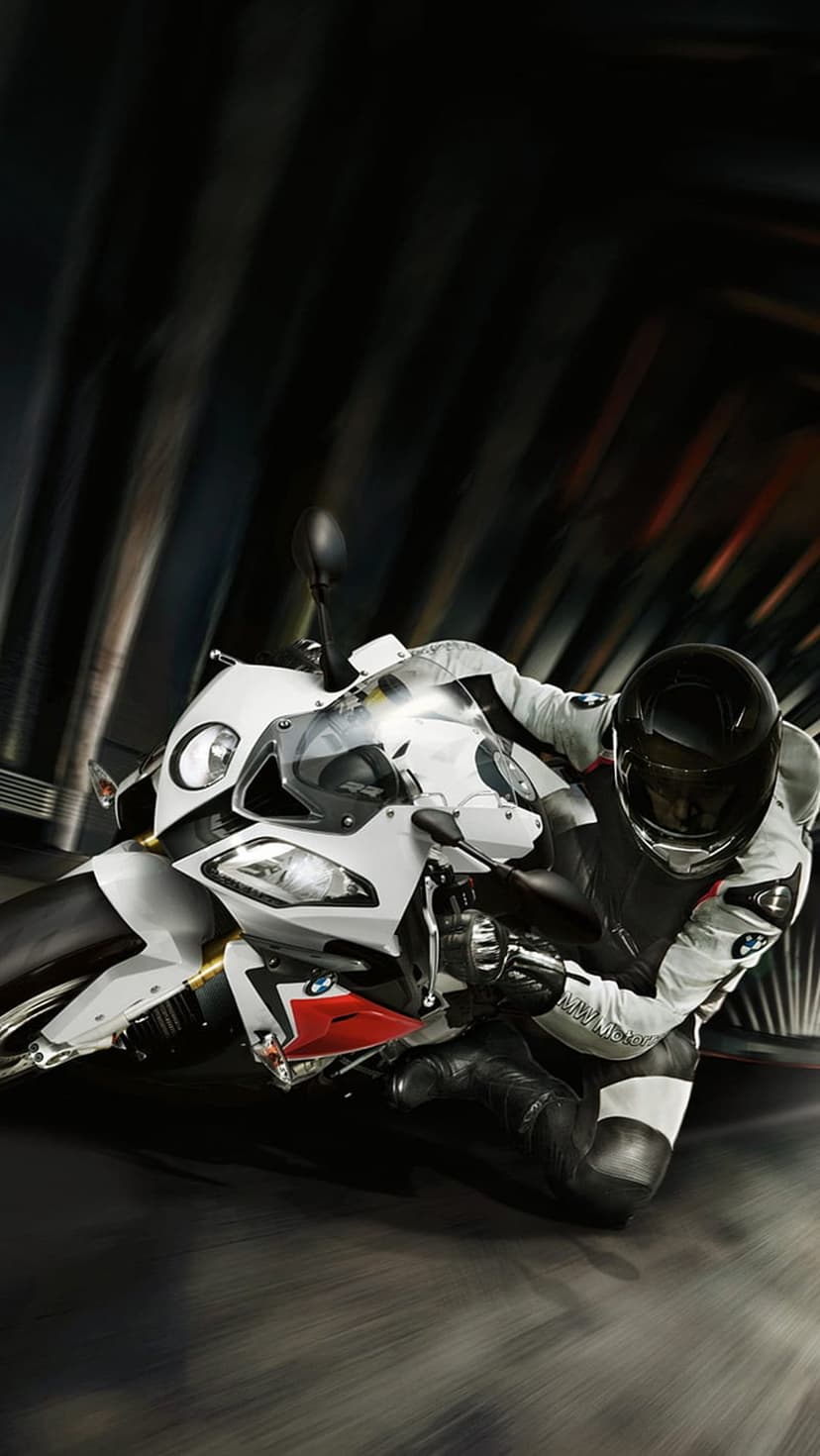 Motorcyclist in white racing gear banks a sleek sportbike into a turn against a blurred track background.