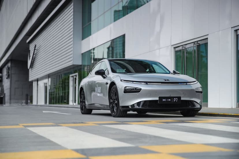 Silver Xpeng P7 electric sedan parked on an urban street with modern white buildings and a crosswalk.