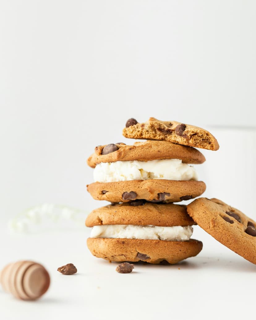 Chocolate chip ice cream sandwiches stacked high with melting vanilla cream and scattered dark chocolate pieces.