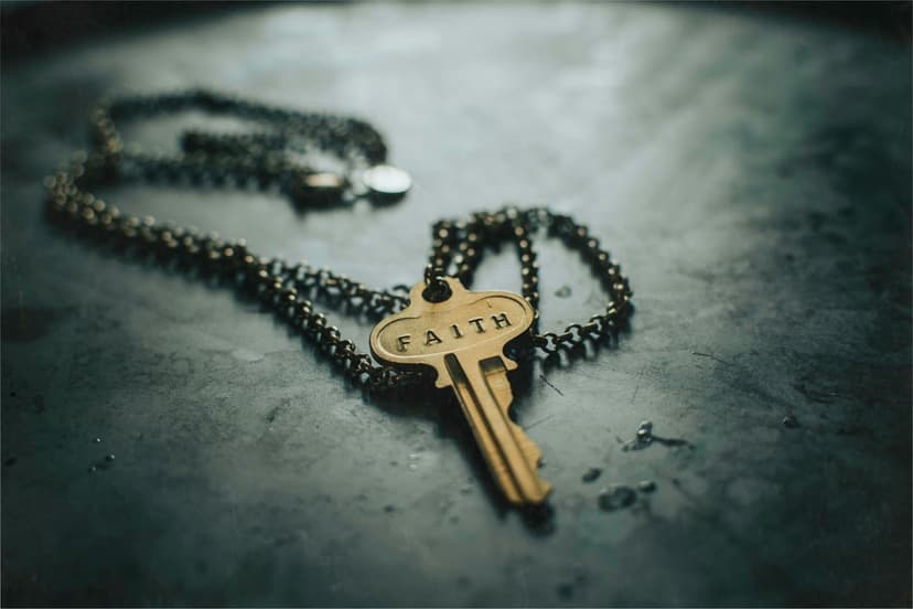 Golden key pendant with faith engraving on a dark textured metallic surface with a blurred dark chain backdrop.