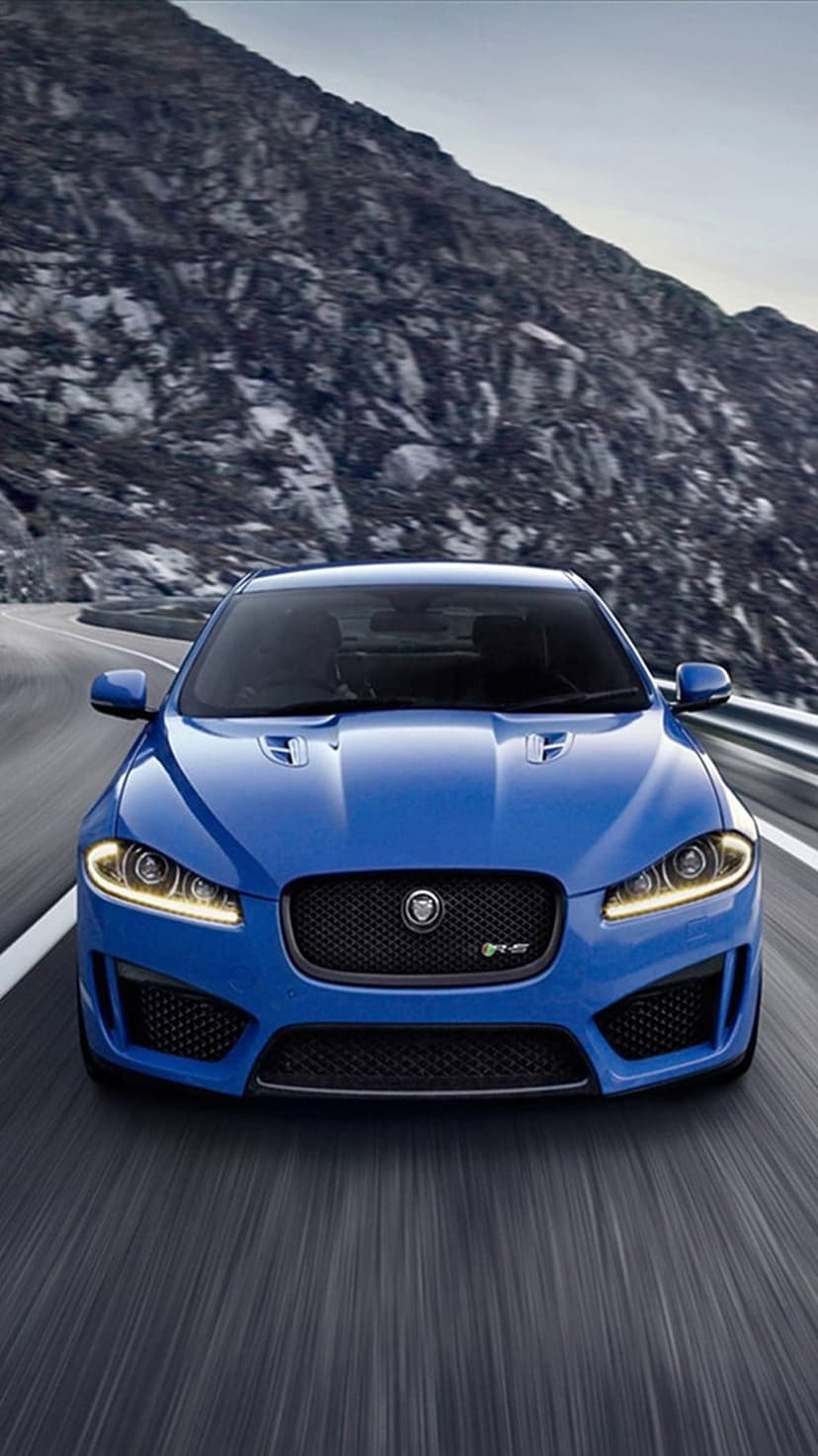 Blue Jaguar F-Type R sports car maneuvers through a winding mountain road with motion-blurred rocky scenery.