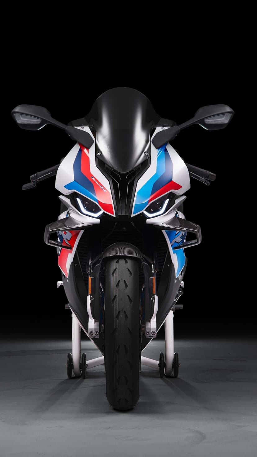 Front view of a white BMW M 1000 RR sportbike with red and blue accents and carbon fiber winglets.
