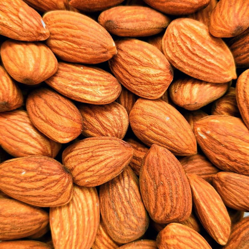 Raw almonds with textured brown skins are piled together in a high-angle macro shot showing natural ridges.
