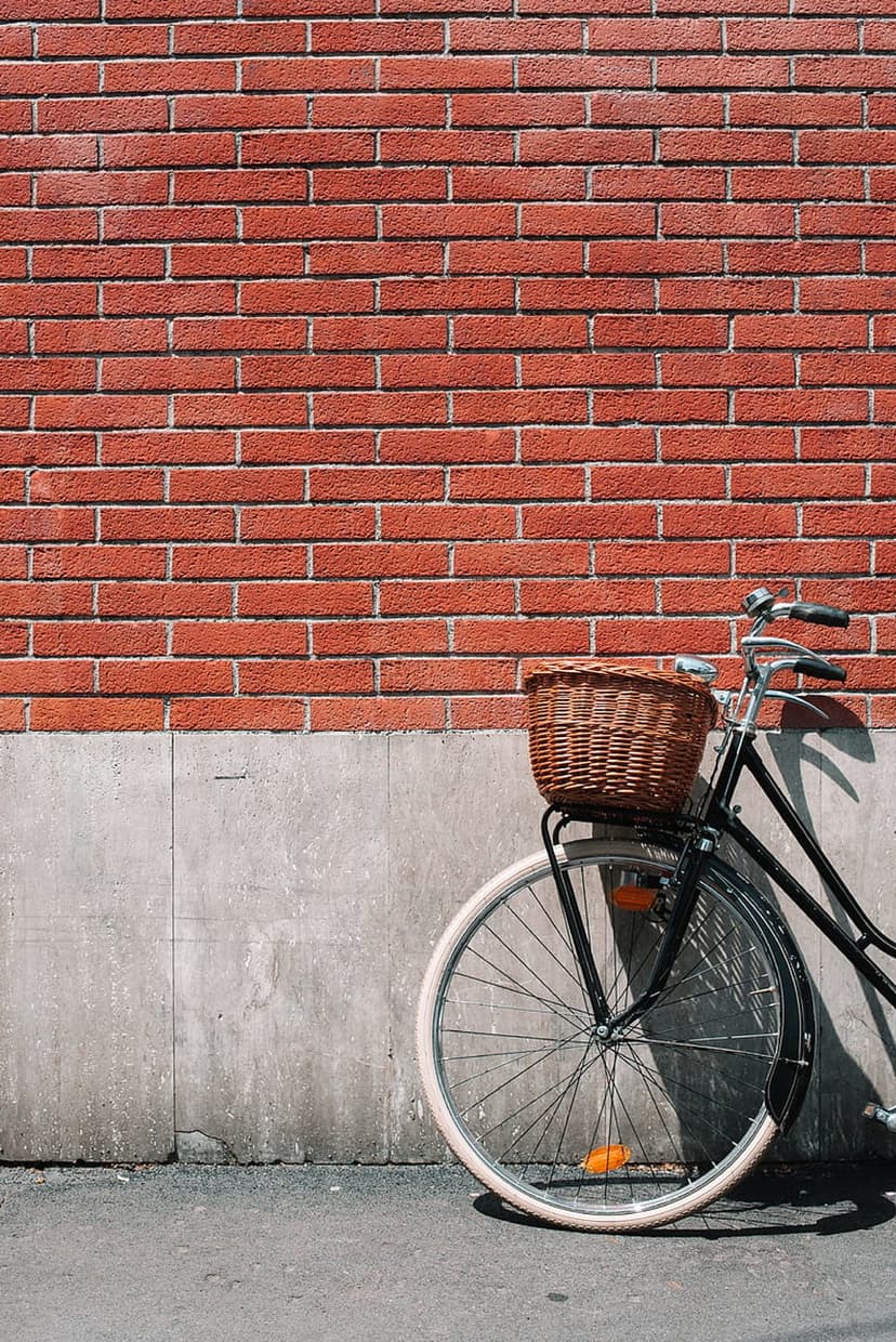 Black bicycle with a wicker basket leaning on a red brick wall under bright sunlight with sharp shadows.