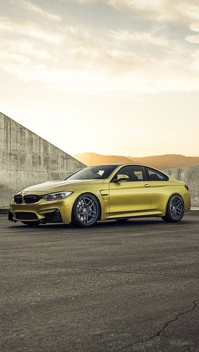 Yellow BMW M4 Coupe parked on asphalt against concrete wall