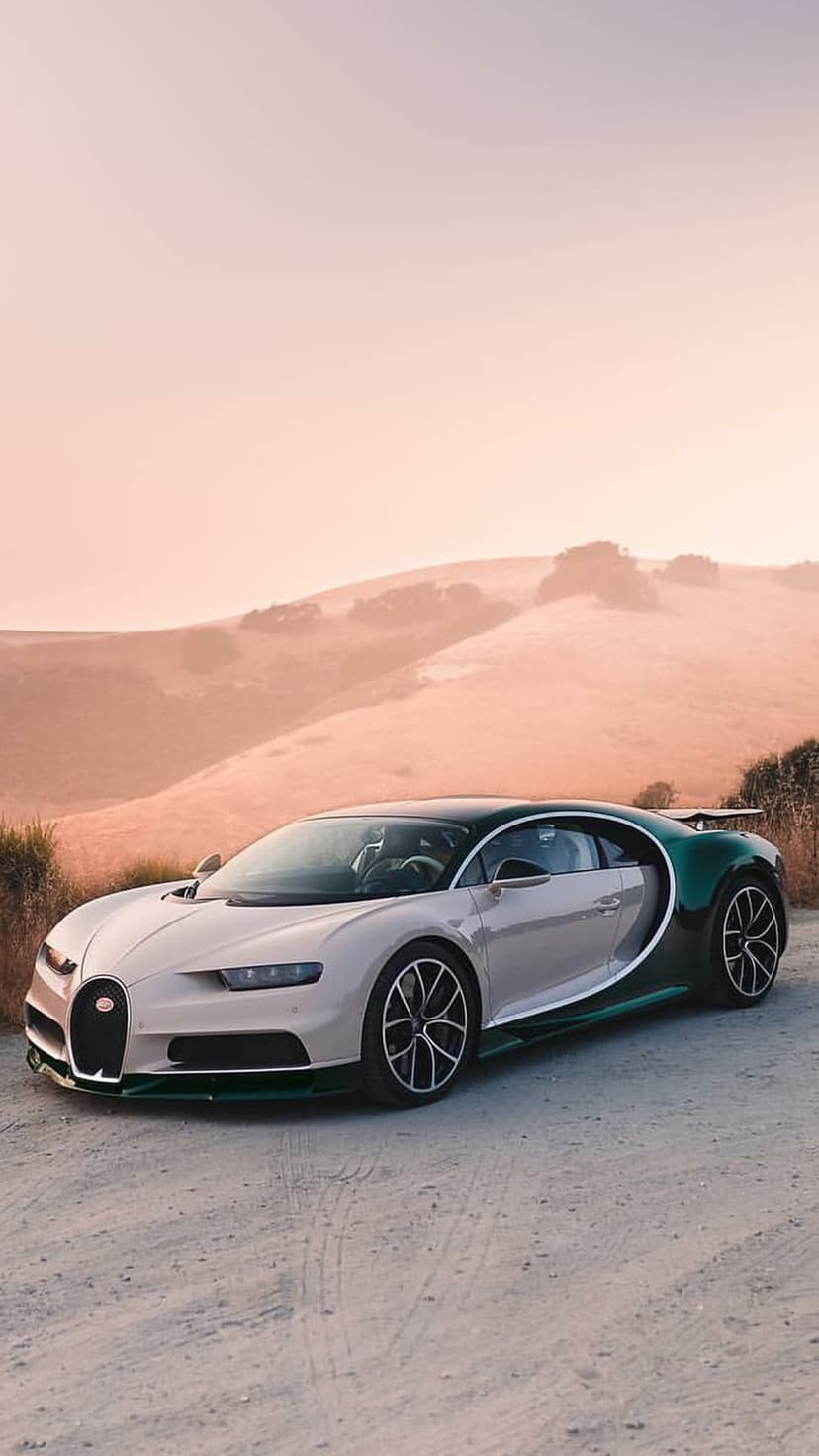 Bugatti Chiron in emerald and beige parked on a dirt road against rolling hills under a purple sunset sky.