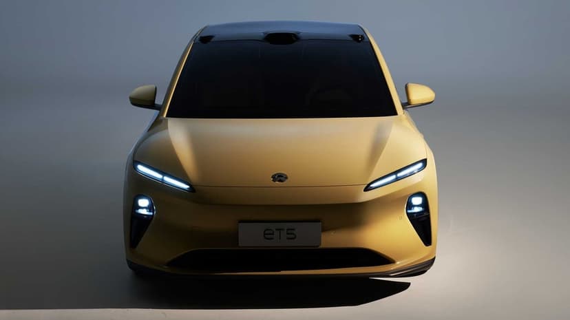 Yellow NIO ET5 electric sedan front view with glowing LED headlights and roof-mounted sensors in a studio.