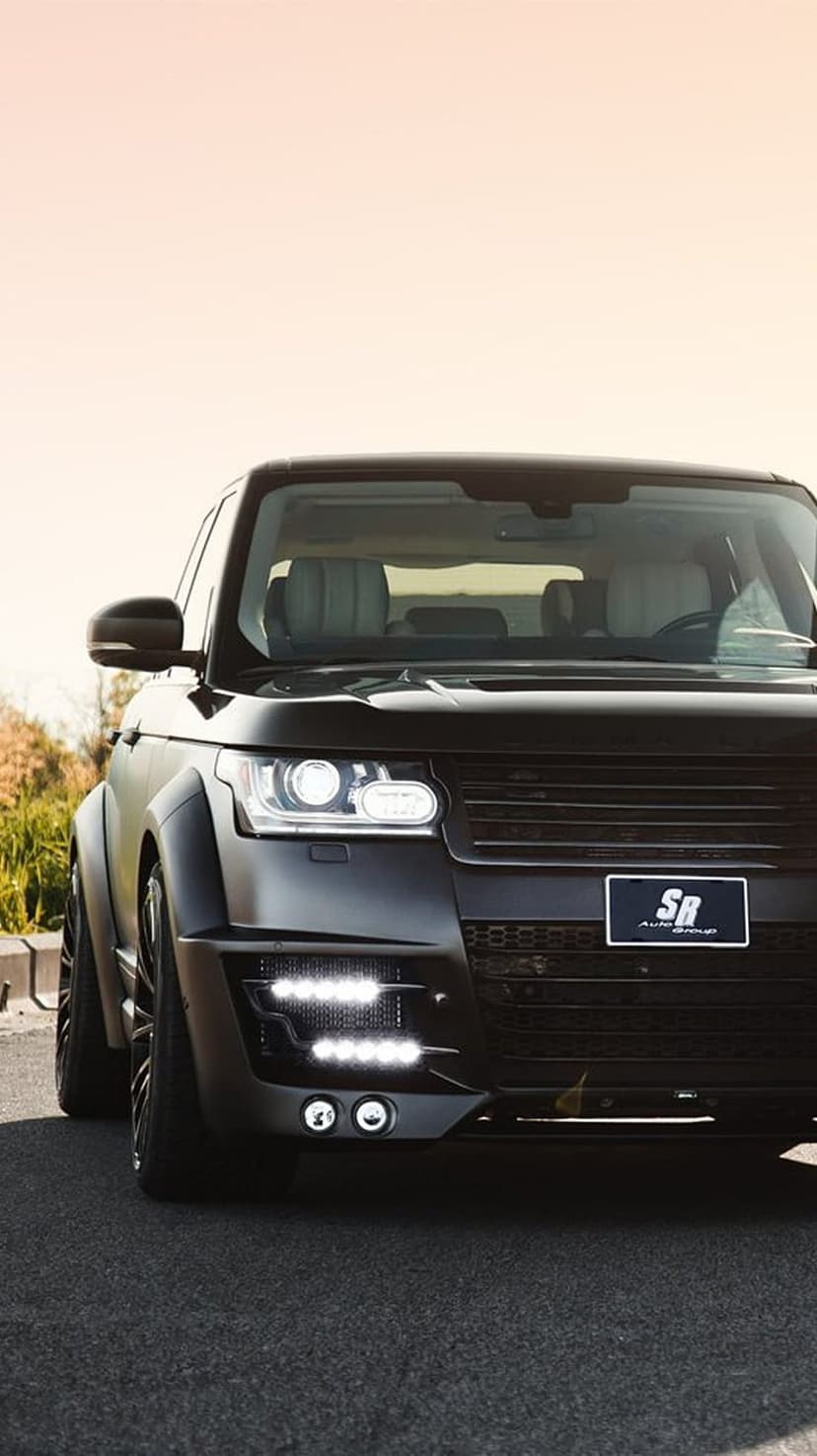 Matte black Range Rover SUV showing custom front grille, LED headlights, and body kit on paved ground.