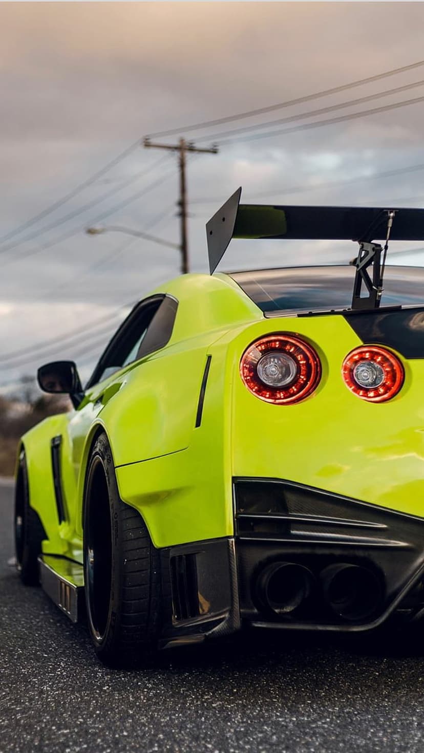 Yellow Nissan GT-R with a wide body kit and massive rear wing parked on asphalt under a cloudy sky.