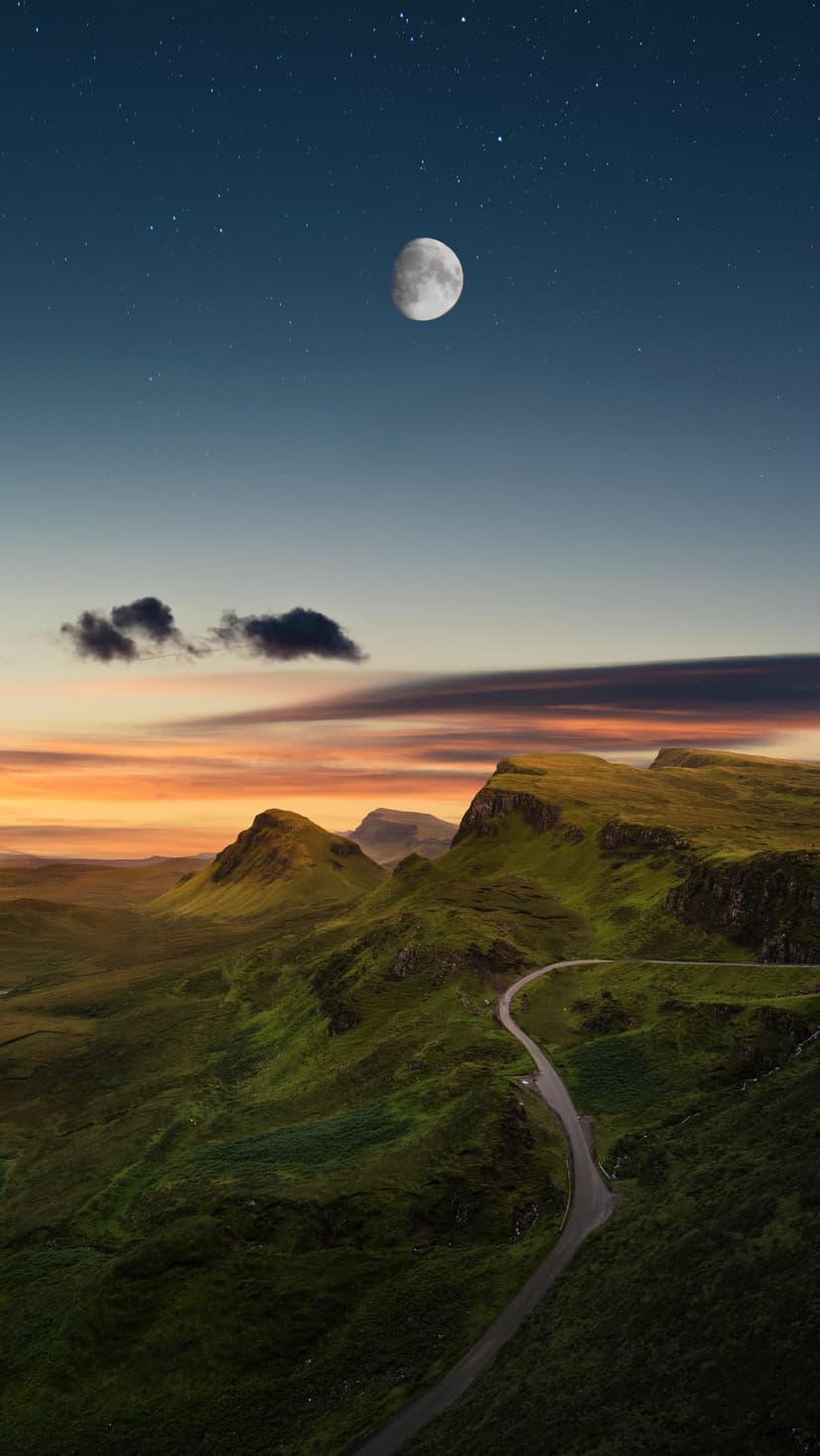 Winding road through green highlands under a crescent moon and star-filled sky at dusk with orange horizon light.