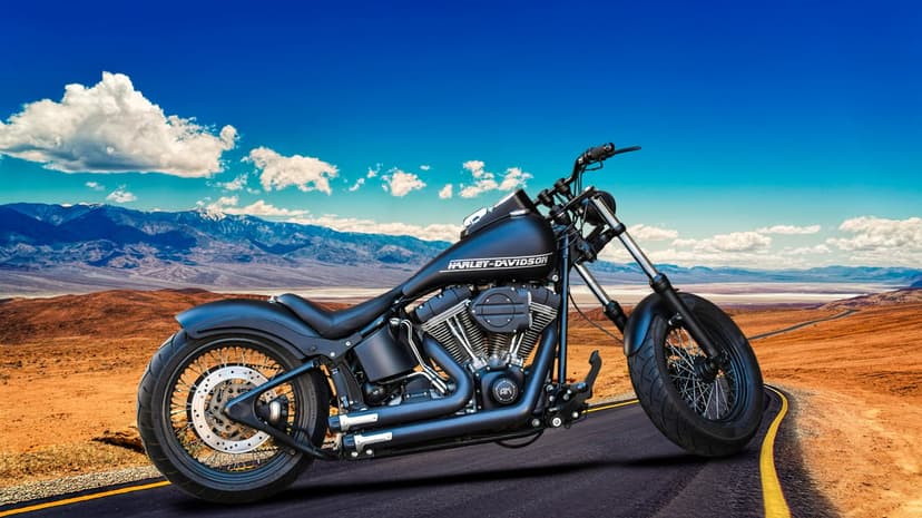 Harley-Davidson motorcycle parked on a desert highway with mountains and white clouds under a bright blue sky.