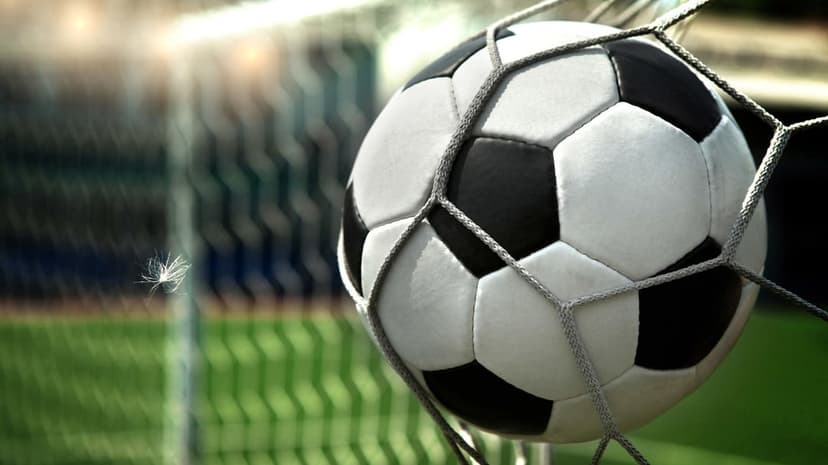 Soccer ball nestled in white nylon netting with glowing stadium lights creating a bokeh effect in the background.