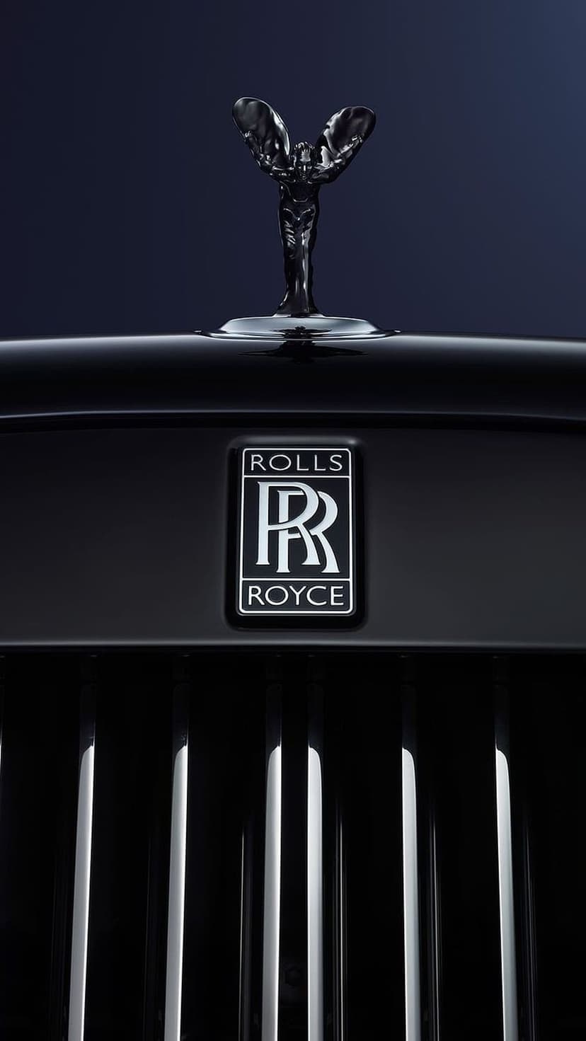Spirit of Ecstasy hood ornament and silver emblem mounted on a dark chrome radiator grille of a luxury car.