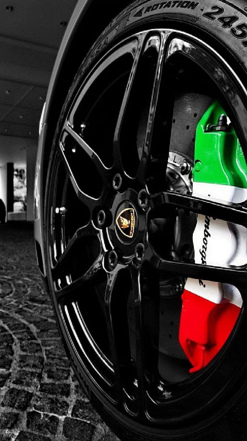 Lamborghini wheel with black spokes reveals green and red Italian flag brake calipers on a cobblestone street.