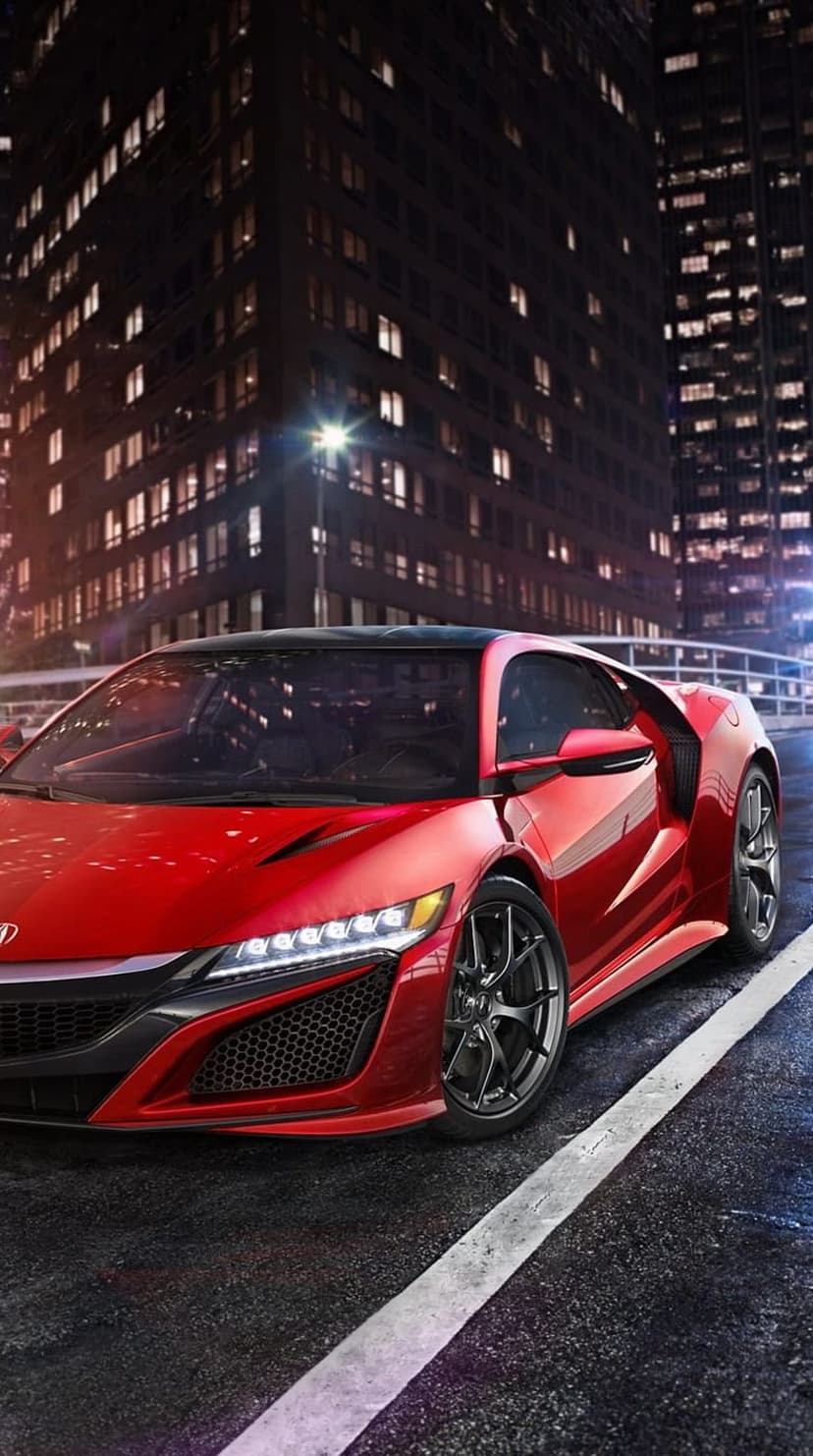 Red sports car parked on a wet city street at night with reflections of neon lights and skyscrapers in the background.