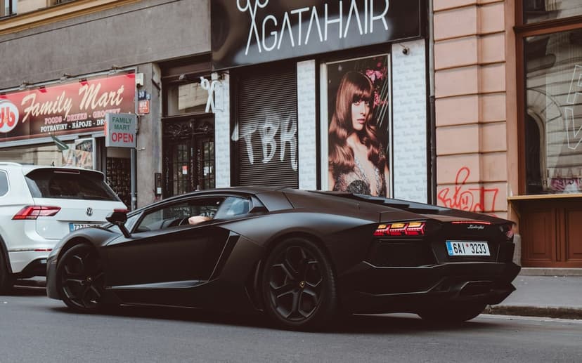 Matte black Lamborghini Aventador parked on an urban street near a Family Mart store and a local hair salon.