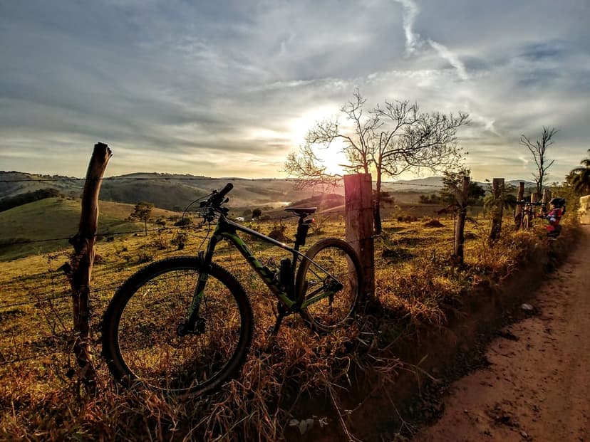 Mountain bike silhouette leaning on a wooden fence post during a golden sunset with rolling hills in background.