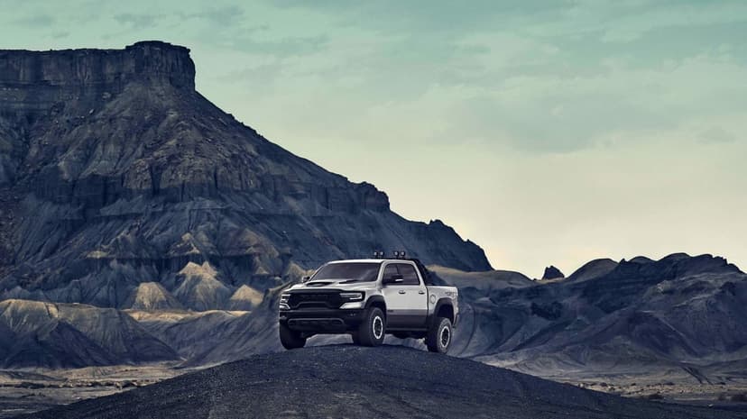 Silver RAM 1500 TRX truck parked on a dark rocky hill with layered mountains under a cloudy sky.