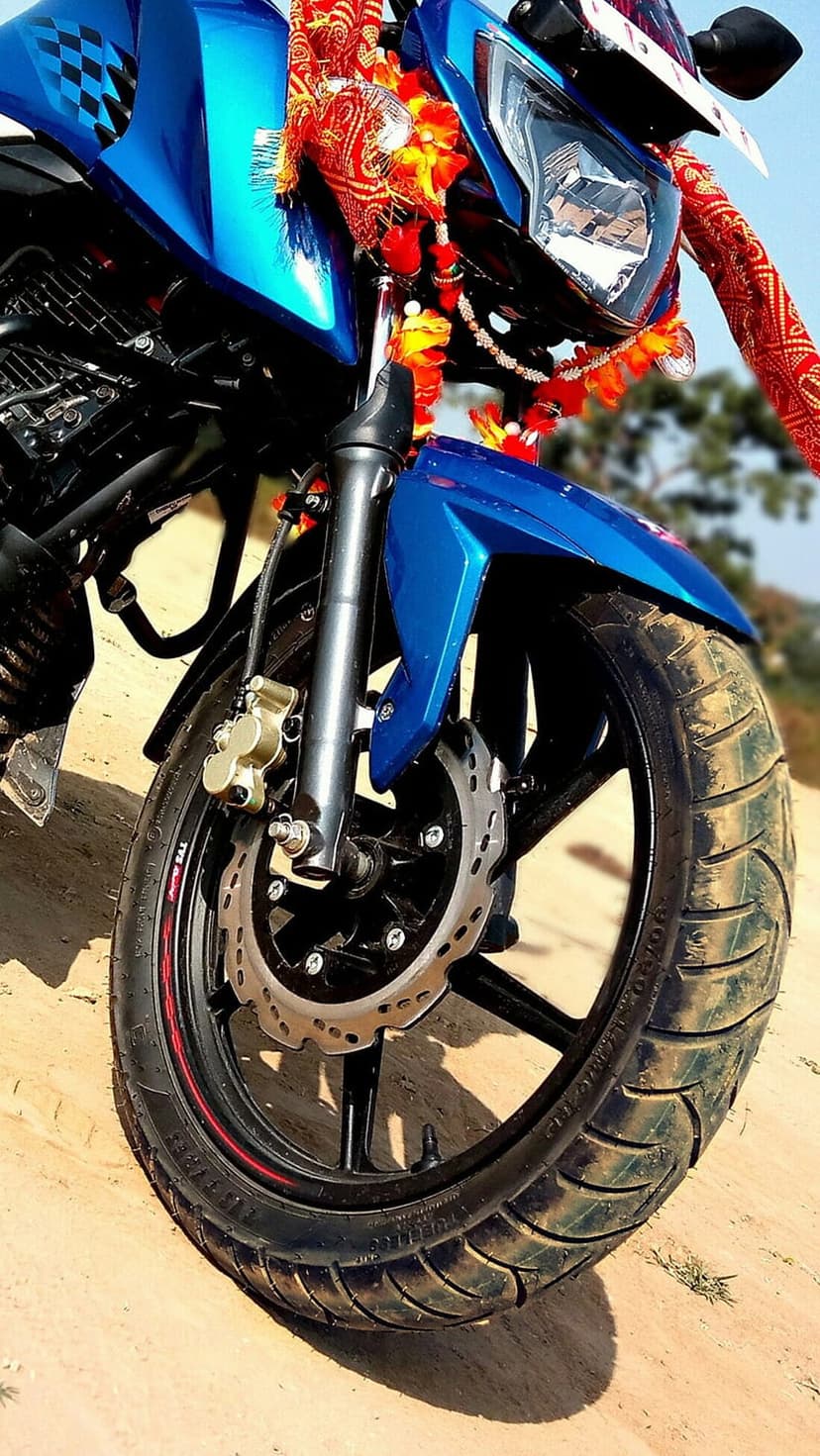 Blue motorcycle front wheel and suspension forks decorated with colorful festive garlands on a sandy surface.
