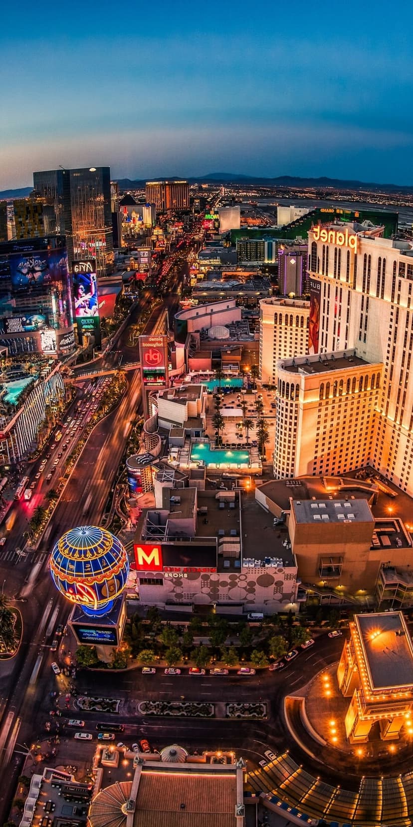 Las Vegas Strip hotels and the High Roller wheel glow with neon lights under a twilight sky at dusk.