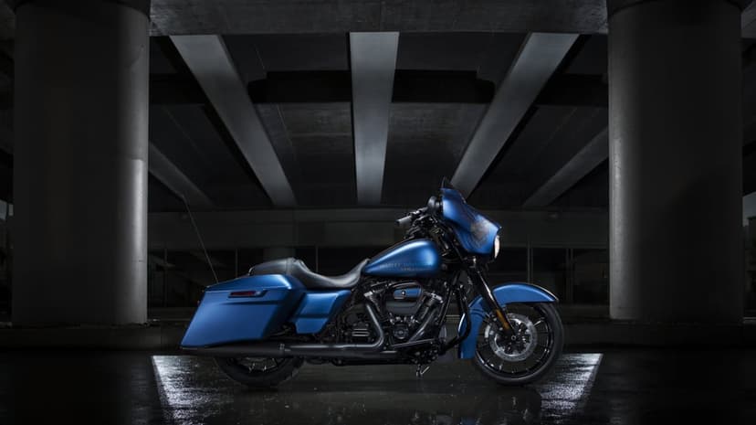 Matte blue motorcycle parked under concrete pillars with dramatic lighting and reflections on wet ground.