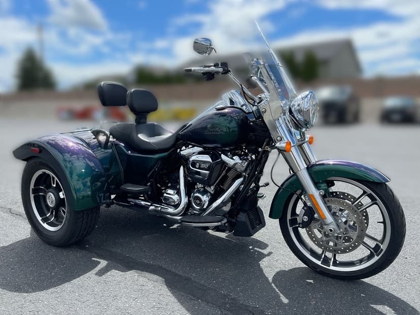 Emerald green and purple iridescent Harley-Davidson trike with chrome engine parked on asphalt under a blue sky.