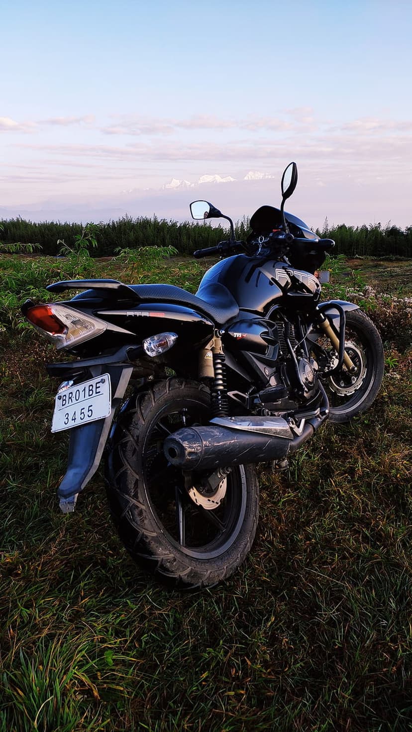 Black motorcycle parked in a grassy field under a pink and blue sunset sky with soft clouds in the background.