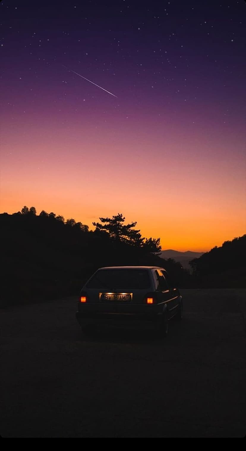 Car with glowing taillights parked on a road under a purple starry sky with a bright shooting star and mountains.