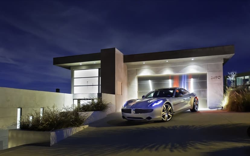Silver sports car with blue headlights parked in front of a modern minimalist house under a dark blue night sky.