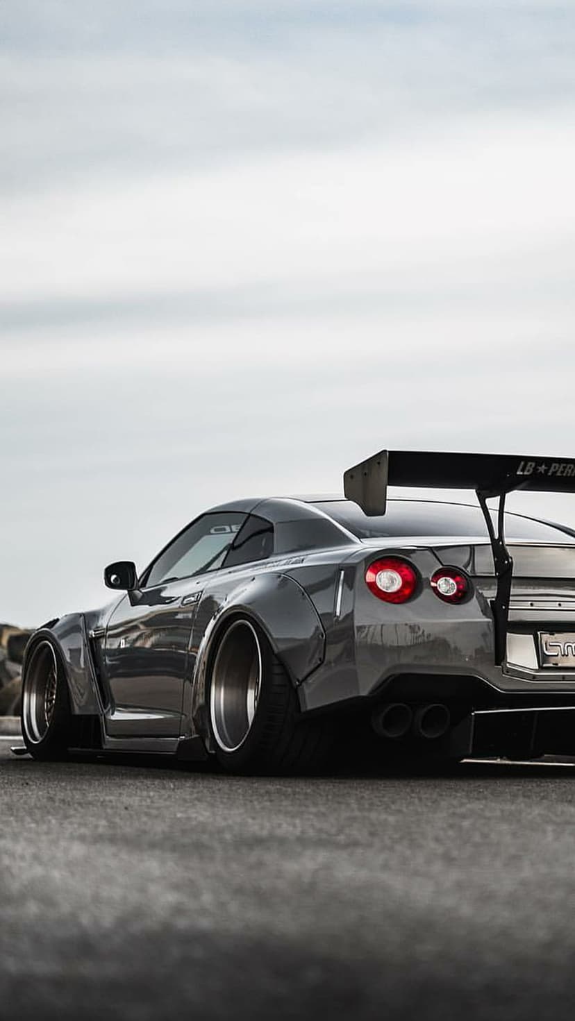 Nissan GTR widebody featuring a large rear wing and signature circular taillights on a low-angle street scene.
