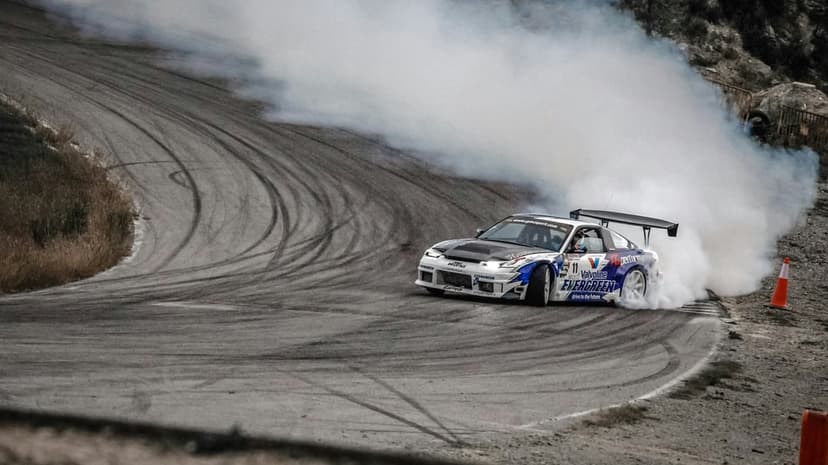 White and blue drift car sliding sideways on a race track while emitting a large cloud of thick white smoke.