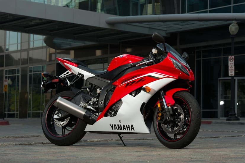 Red and white Yamaha R6 motorcycle parked on pavement in front of a modern glass building with reflections.