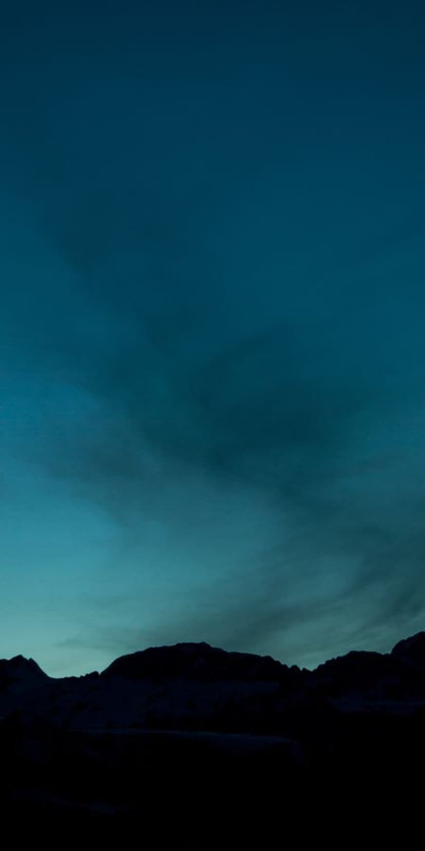 Jagged mountain silhouettes stand against a twilight gradient sky transitioning from dark navy blue to soft teal.