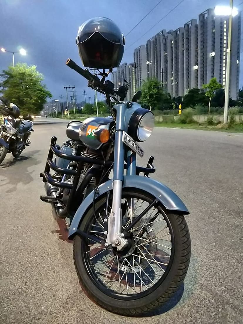 Royal Enfield motorcycle with a black helmet on the handlebars parked on a city road against twilight buildings.