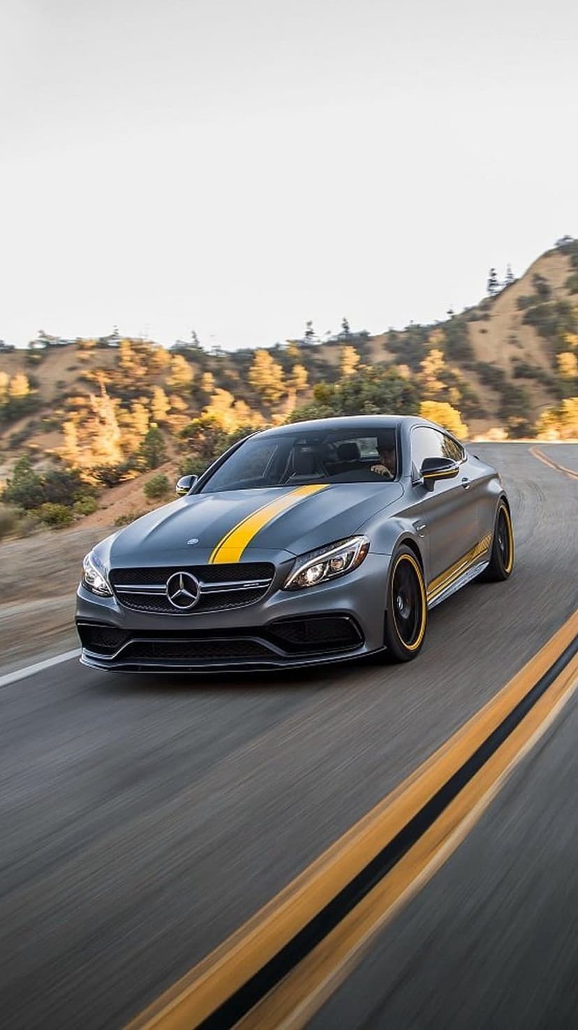 Mercedes-AMG C63 Coupe with yellow racing stripes drives on a winding mountain road under bright sunlight.